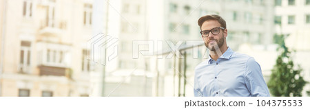 Young handsome caucasian businessman with suitcase waiting for taxi outdoors, standing on city street and looking away Young handsome caucasian businessman with suitcase waiting for taxi outdoors, standing on city street and looking away 104375533