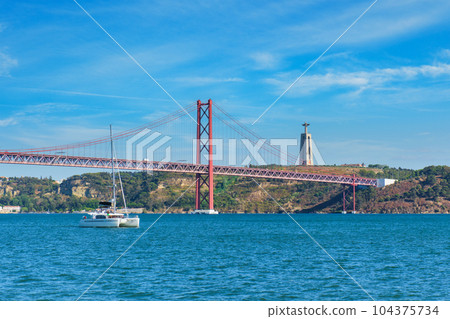 View of 25 de Abril Bridge famous tourist landmark over Tagus river, Christ the King monument and a tourist yacht boat. Lisbon, Portugal 104375734