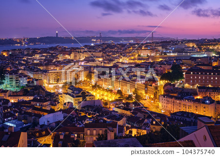 Night view of Lisbon famous view from Miradouro da Senhora do Monte tourist viewpoint of Alfama and Mauraria old city districts, 25th of April Bridge in the evening twilight. Lisbon, Portugal 104375740
