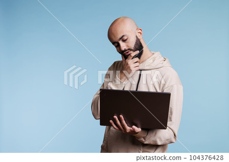 Thoughtful arab man rubbing chin in doubt while working on laptop. Young pensive person with puzzled expression thinking while holding portable computer and analyzing business data Thoughtful arab man rubbing chin in doubt while working on laptop. Young pensive person with puzzled expression thinking while holding portable computer and analyzing business data 104376428