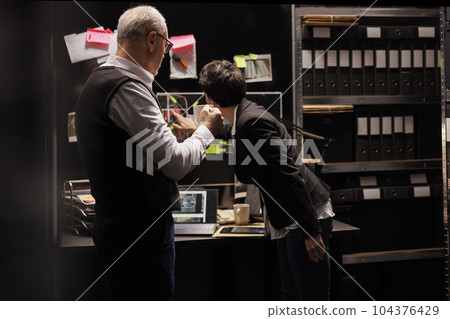 Private detectives working overhours at crime report in federal bureau, discussing criminal investigations evidence. Fbi agents analyzing mysterious suspect information, planning strategy to catch him 104376429