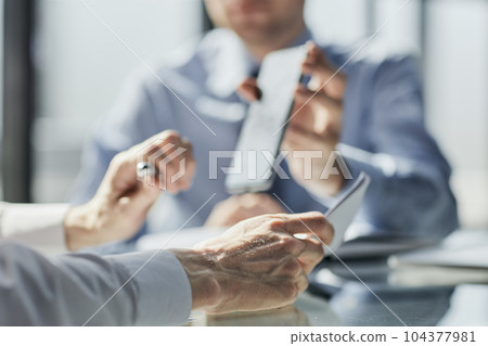 Two business men sit at desk discuss project details Two business men sit at desk discuss project details 104377981