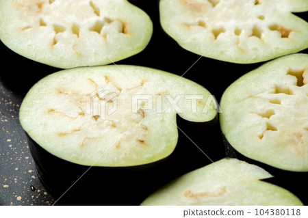 A cooking scene where eggplants are cut into round slices and baked in a frying pan. (Irregularly shaped eggplants harvested from a kitchen garden.) 104380118