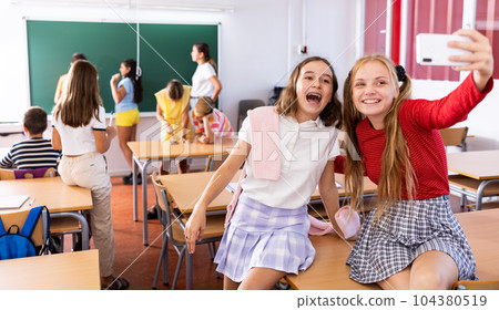 Happy schoolgirls taking selfie with phone at recess between lessons 104380519