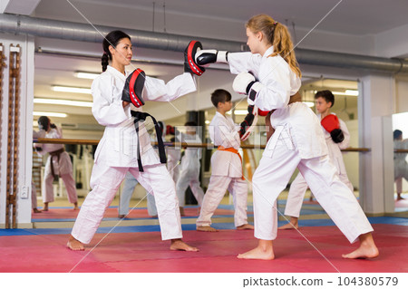 Female trainer in boxing gloves conducts sparring and teaches punches to girl in karate and self-defense training Female trainer in boxing gloves conducts sparring and teaches punches to girl in karate and self-defense training 104380579