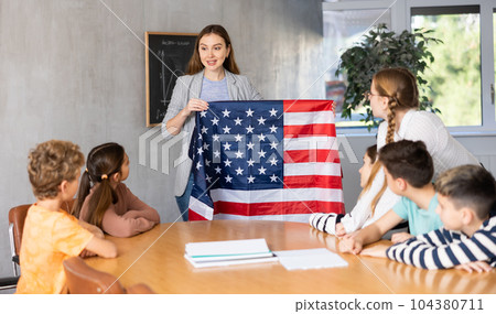 Geography lesson in school class - teacher talks about United States of America, holding flag in his hands Geography lesson in school class - teacher talks about United States of America, holding flag in his hands 104380711