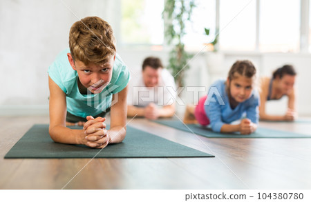 Diligent preteen boy practicing plank pose of yoga with his family Diligent preteen boy practicing plank pose of yoga with his family 104380780