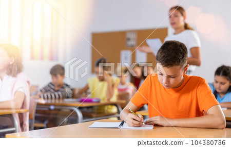 Focused preteen schoolboy writing in workbook during lesson 104380786