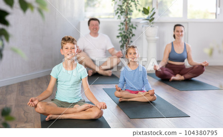 Teenage girl with her parents practices yoga in lotus position Teenage girl with her parents practices yoga in lotus position 104380795
