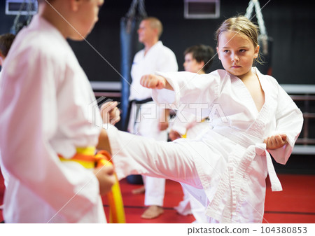 Children practicing in pair karate movements with male trainer supervision 104380853
