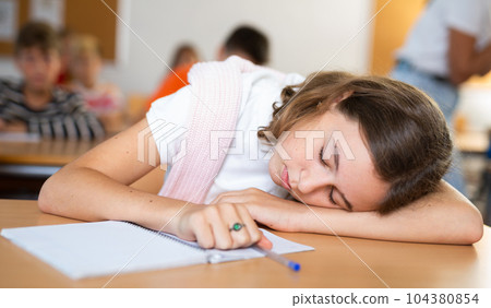 Girl is tired and sleeping at the desk in classroom 104380854
