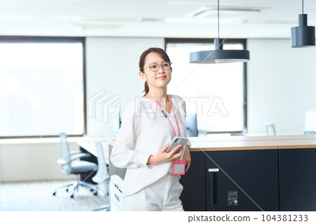 A woman standing in the office with a smartphone 104381233