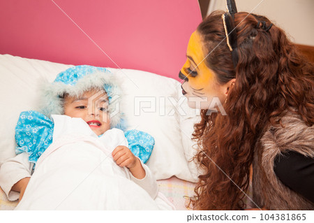 Little girl playing grandma character and mother playing wolf. Real family having fun while using costumes of the Little red riding hood tale in Halloween. Little girl playing grandma character and mother playing wolf. Real family having fun while using costumes of the Little red riding hood tale in Halloween. 104381865