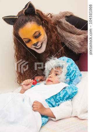 Little girl playing grandma character and mother playing wolf. Real family having fun while using costumes of the Little red riding hood tale in Halloween. Little girl playing grandma character and mother playing wolf. Real family having fun while using costumes of the Little red riding hood tale in Halloween. 104381866