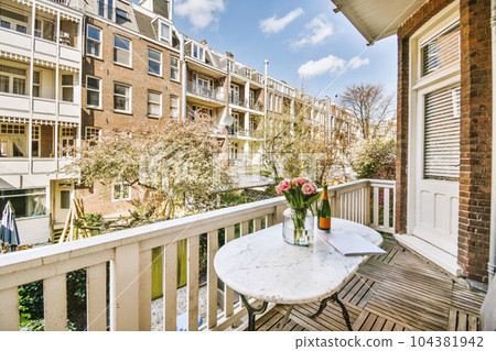 a balcony with flowers in a vase on the table next to an open door that leads out onto the street 104381942