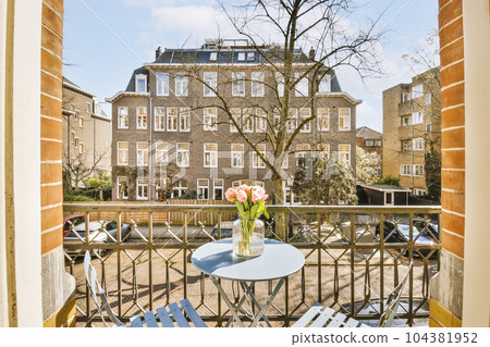 a balcony with two chairs and a table in front of an open window looking out onto the canal from outside 104381952