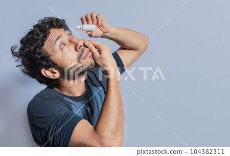 Person applying dropper to irritated eye. People applying refreshing drops to irritated eye. Man putting a dropper in his eye isolated. Man with irritated eye applying drops with a dropper Person applying dropper to irritated eye. People applying refreshing drops to irritated eye. Man putting a dropper in his eye isolated. Man with irritated eye applying drops with a dropper 104382311