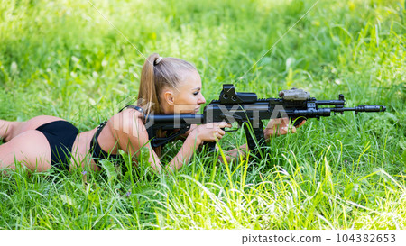 Caucasian woman in bikini lies with machine gun on green grass. Caucasian woman in bikini lies with machine gun on green grass. 104382653