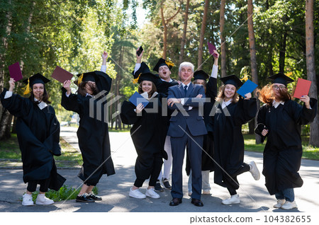 A university professor and seven robed graduates are jumping outdoors. 104382655