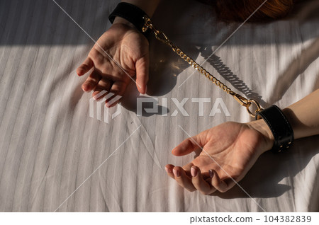 Close-up of woman's hands in leather handcuffs. Sex toy. Close-up of woman's hands in leather handcuffs. Sex toy. 104382839