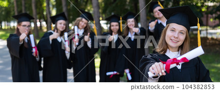 Happy young caucasian woman celebrating graduation with classmates. A group of graduate students outdoors. Widescreen. Happy young caucasian woman celebrating graduation with classmates. A group of graduate students outdoors. Widescreen. 104382853