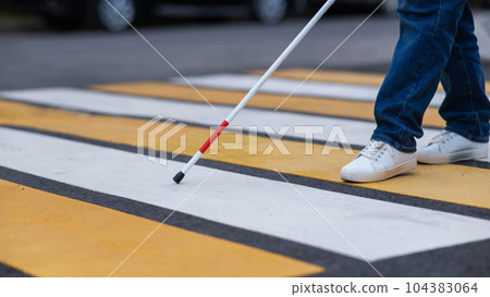 Close-up of the legs of a blind woman crossing the road at a crosswalk with a cane. Close-up of the legs of a blind woman crossing the road at a crosswalk with a cane. 104383064