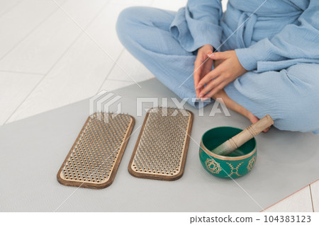 Asian woman sitting on yoga mat with tibetan singing bowl and sadhu boards. Asian woman sitting on yoga mat with tibetan singing bowl and sadhu boards. 104383123