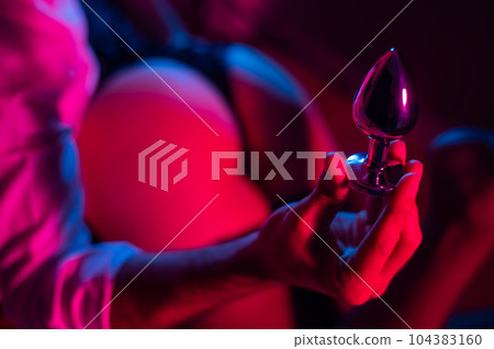 A man with a mistress on his knees holds an anal plug in the bedroom. 104383160