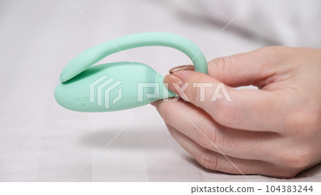 Woman holding mint vibrator while lying on white sheet. Woman holding mint vibrator while lying on white sheet. 104383244