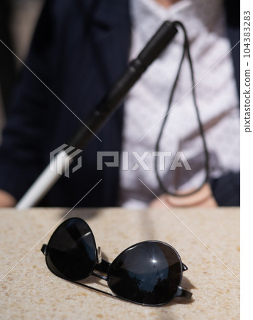 A blind woman in a business suit is sitting in an outdoor cafe.  104383283