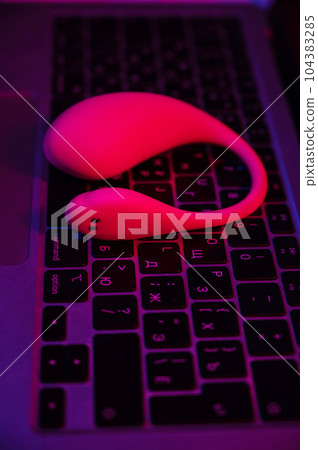 Close-up of a curved vibrator on a laptop keyboard in blue-red light. Close-up of a curved vibrator on a laptop keyboard in blue-red light. 104383285