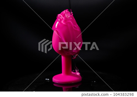 Pink anal plug in intimate lubricant on a black background.  104383298