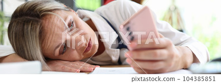 Tired doctor putting head on table and surfing internet on smartphone 104385851