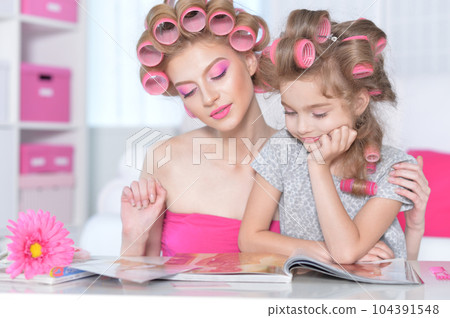 Mom and daughter with hair curlers reading magazine Mom and daughter with hair curlers reading magazine 104391548