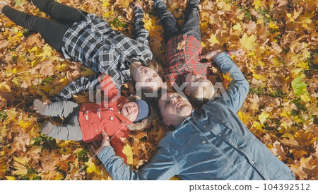 The happy family lies on their backs in the autumn leaves. 104392512