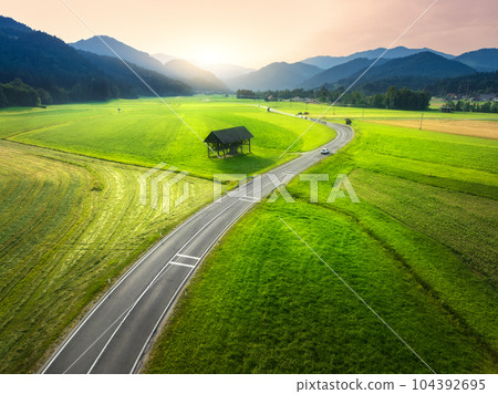 Aerial view of road in green meadows at sunset in summer Aerial view of road in green meadows at sunset in summer 104392695