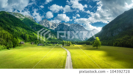 Aerial view of road in alpine mountains, green meadows, trees 104392728