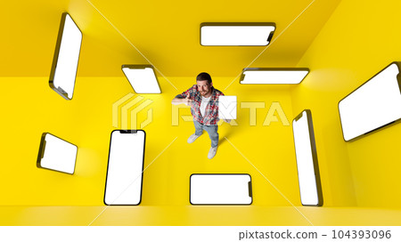 Conceptual design. Man with 3d mobile phone screens over yellowbackground. Online shopping and services. E-commerce Conceptual design. Man with 3d mobile phone screens over yellowbackground. Online shopping and services. E-commerce 104393096
