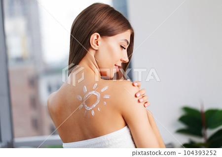 Happy young woman wrapped in towel using body nourishing cream or lotion. Happy young woman wrapped in towel using body nourishing cream or lotion. 104393252