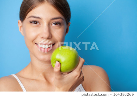 Young woman with snow-white smile holding green apple, teethcare. 104393269