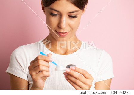 A young woman puts on contact lenses in her apartment 104393283