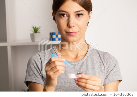 A young woman puts on contact lenses in her apartment 104393302