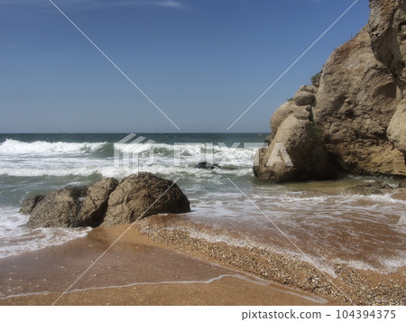 View of the rocky seashore. Fantastic view of the rocky shore on a sunny day with blue sky. A picturesque and magnificent scene. The concept of active recreation, travel. View of the rocky seashore. Fantastic view of the rocky shore on a sunny day with blue sky. A picturesque and magnificent scene. The concept of active recreation, travel. 104394375
