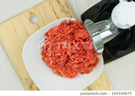 Bowl of mince with electric meat grinder in kitchen interior. Homemade minced meat comes out of the meat grinder. Cooking a burger. 104394675