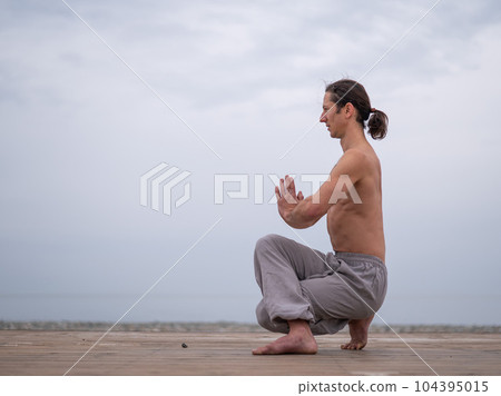 Caucasian man with naked torso practicing wushu on the seashore.  104395015