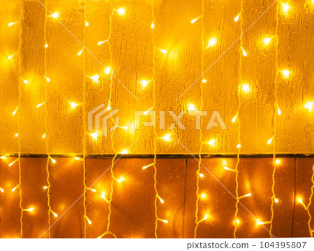Christmas yellow light garlands hang vertically on the wall, soft focus 104395807