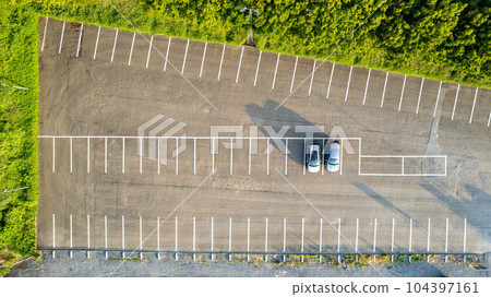 Aerial view of an almost empty parking lots with two parked cars during sunrise, casting long 104397161