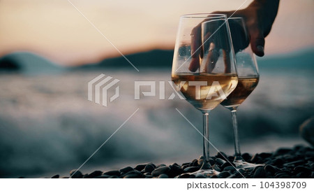 Picking one of two white wine glasses on pebble beach Picking one of two white wine glasses on pebble beach 104398709