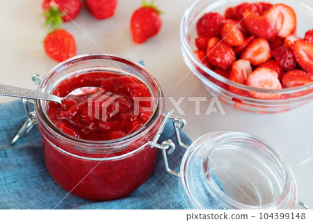 Glass jar with strawberry jam prepared for canning and fresh strawberries in a bowl on the table 104399148