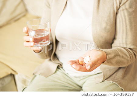 Middle aged unrecognized woman sitting at home, holding glas of fresh water and taking medicine. 104399157
